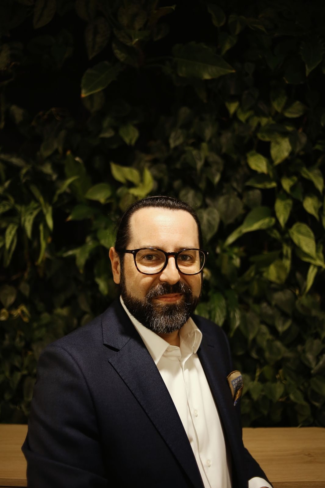 Dariusz Fink-Finowicki w granatowej marynarce, na tle ściany z zielonych liści